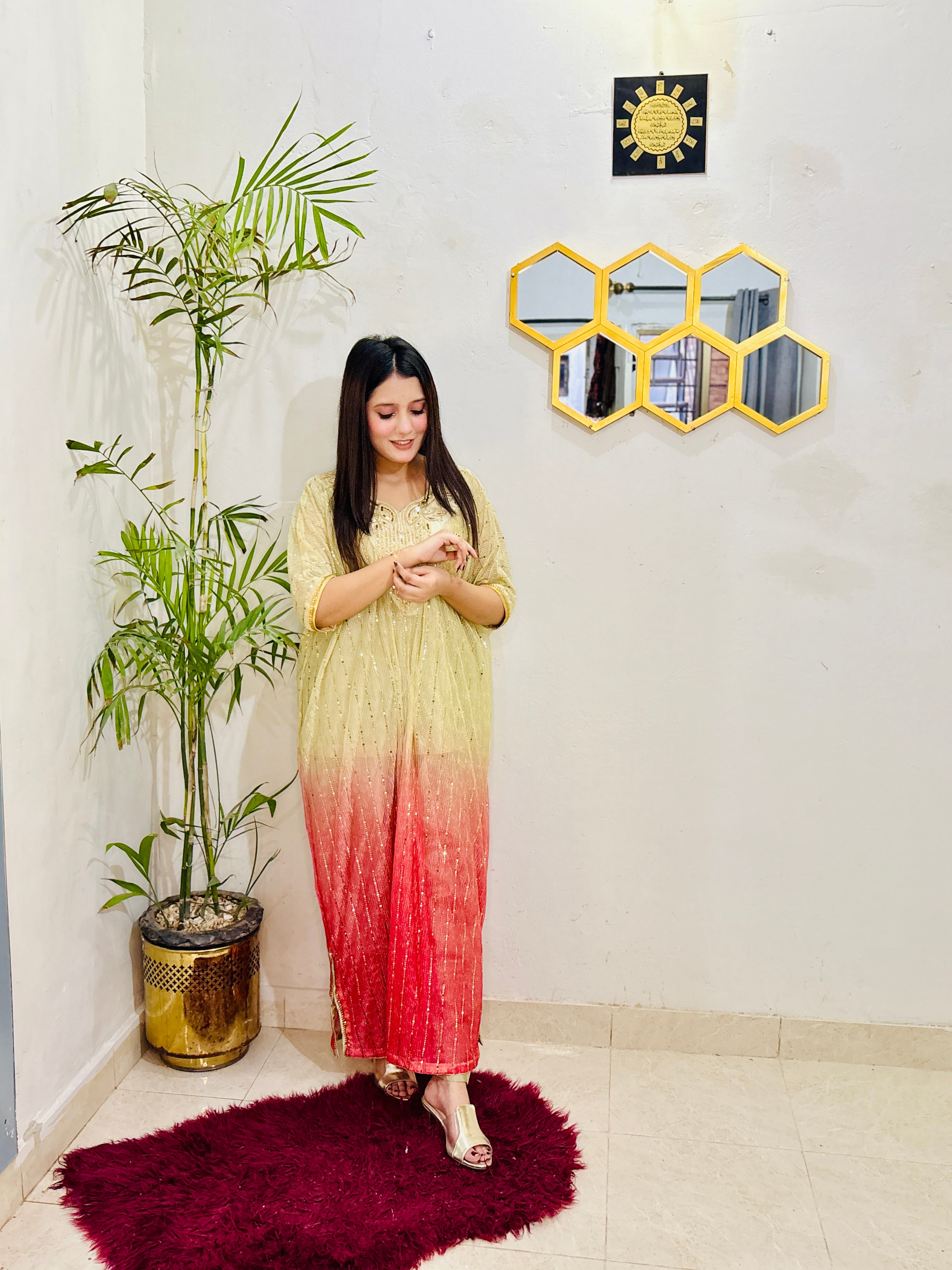 Woman in a gradient dress standing in a room with a plant and wall decor.